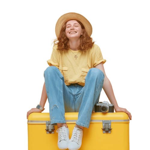 A young woman sits on top of her suitcase while smiling against an isolated solid color background