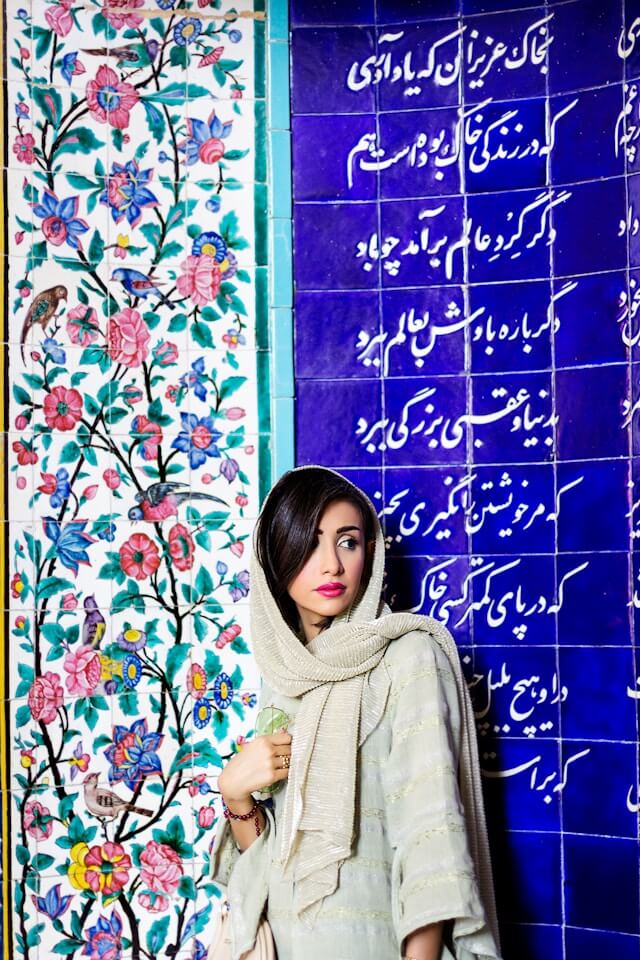 Compassimo-Iranian woman standing in front of a wall with meaningful Persian calligraphy