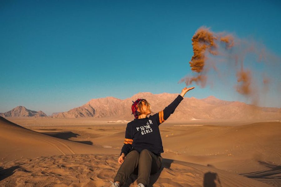 Compassimo-A woman throws sand in Yazd desert, Iran, under a clear blue sky-Lut Desert-Iran-
